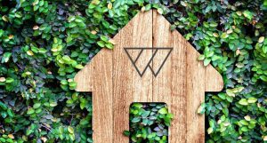A Wondrwall branded wooden house model on a wall of foliage.